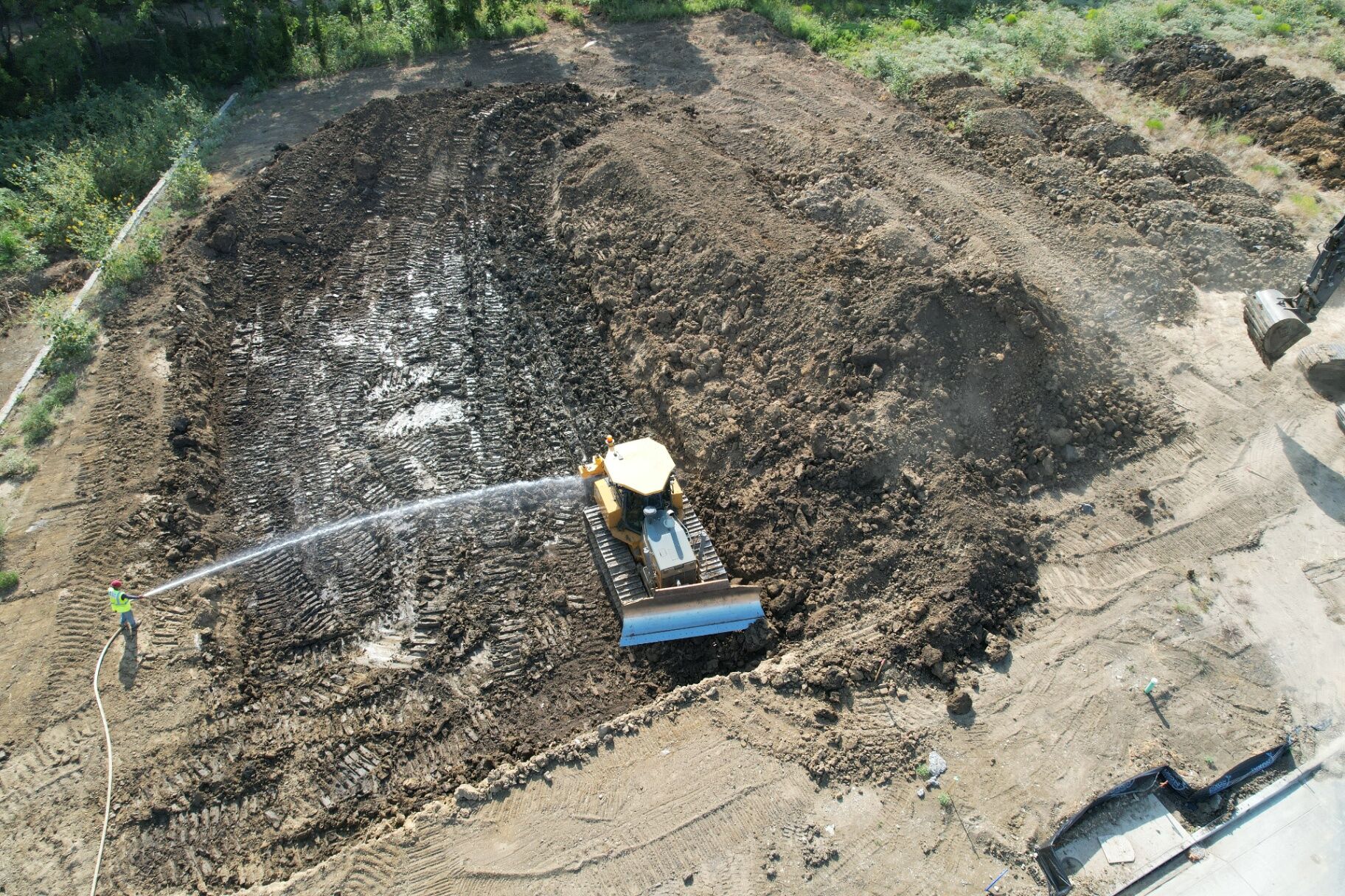 Aerial view of a dozer spreading fill on a building pad while the dirt is watered down