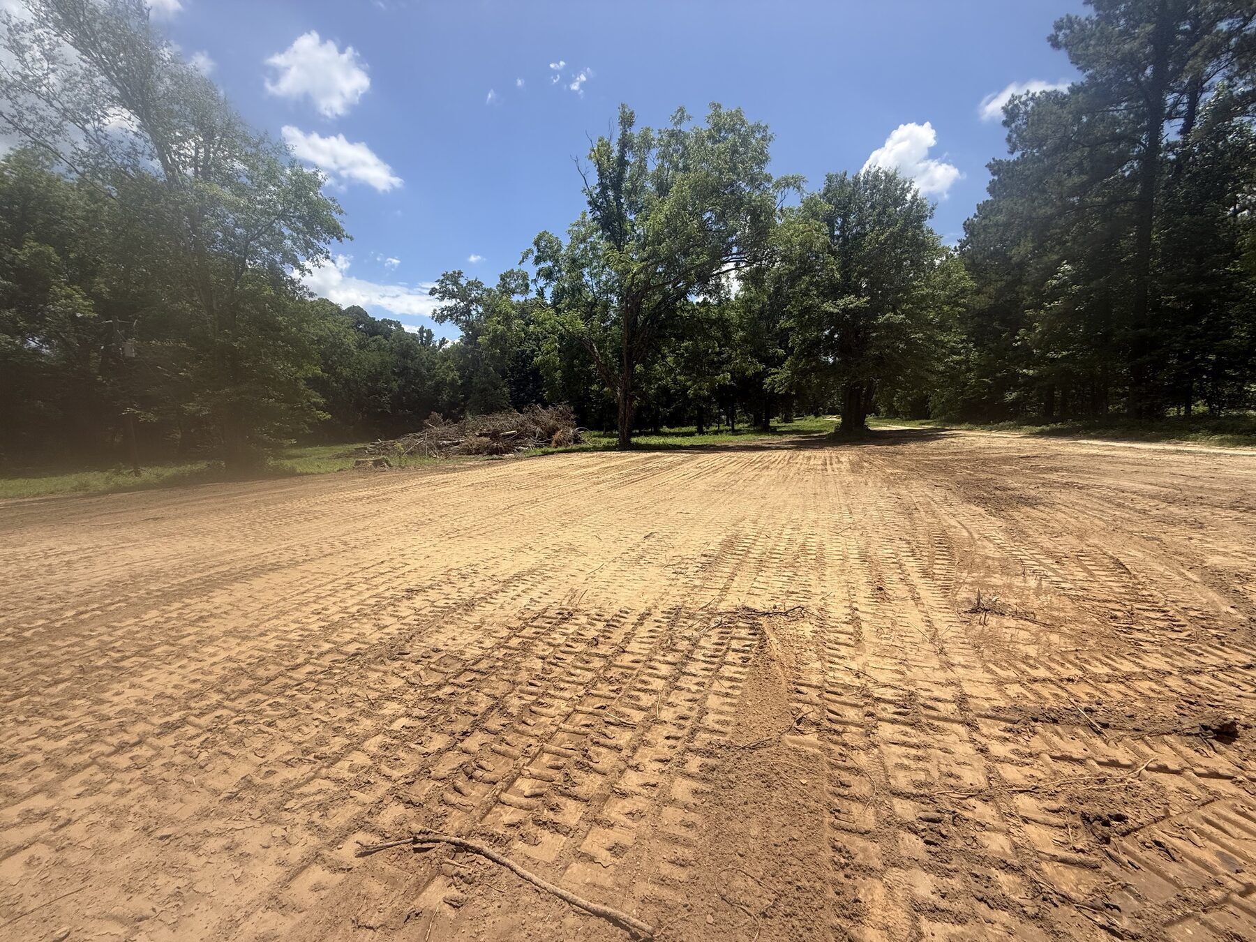 Freshly cleared and tracked-in lot with brush piled at the treeline
